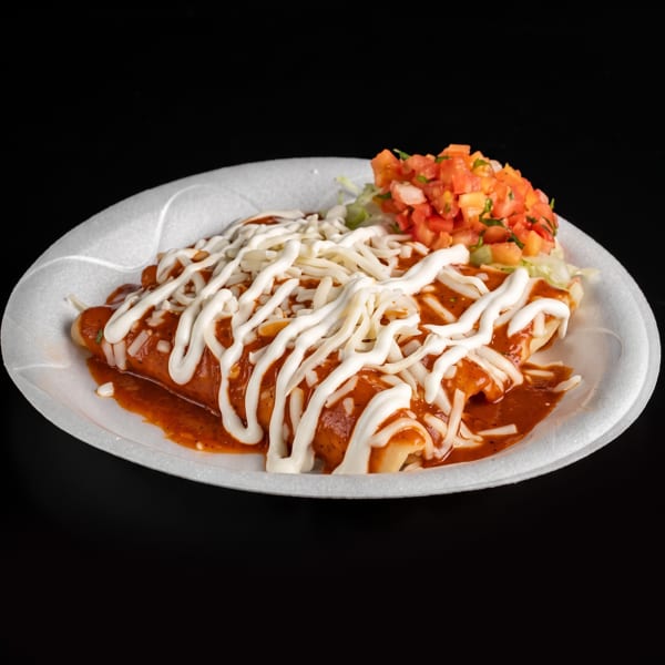Enchiladas covered in red sauce, shredded cheese, and crema, served with fresh tomato salsa on a white plate.