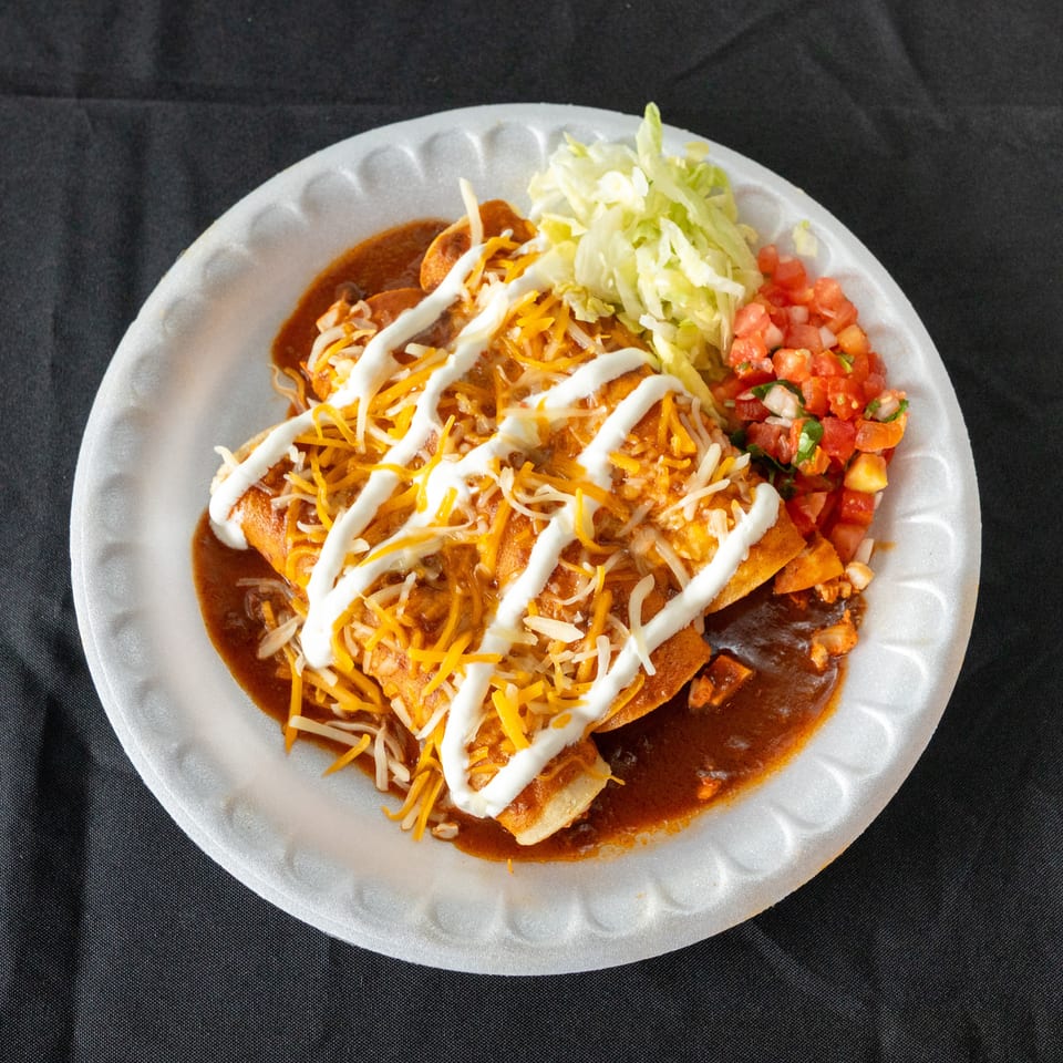 Cheesy enchiladas smothered in red sauce and sour cream, served with shredded lettuce and fresh pico de gallo on a plate.