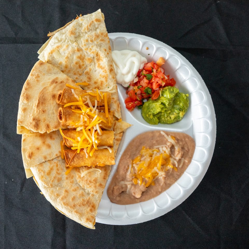Mexican combo plate with flour tortillas, rolled tacos topped with cheese, refried beans, guacamole, salsa, and sour cream.