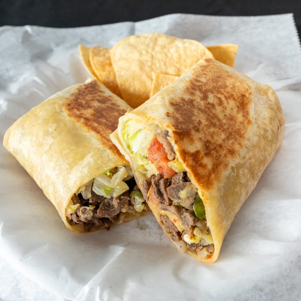 Grilled beef burritos filled with lettuce, tomatoes, onions, and peppers, served with tortilla chips on wax paper.