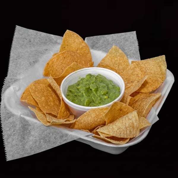 Crispy tortilla chips surround a bowl of chunky guacamole on a lined serving tray.