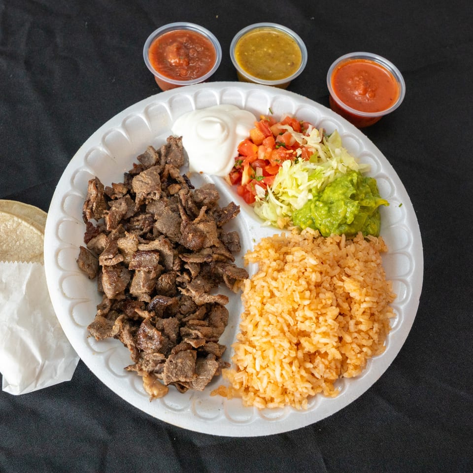 Mexican platter with grilled beef, rice, beans, salad, guacamole, sour cream, tortillas, and three sauces.