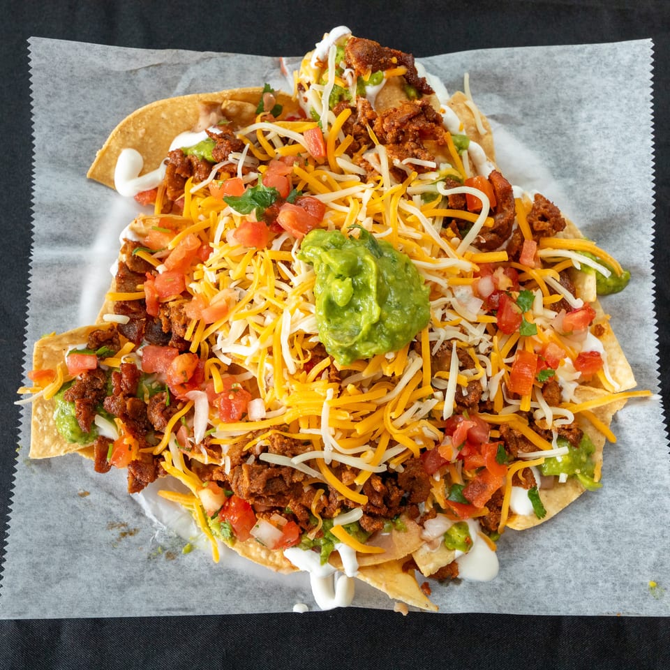 Loaded nachos topped with seasoned meat, melted cheese, guacamole, diced tomatoes, sour cream, and cilantro.